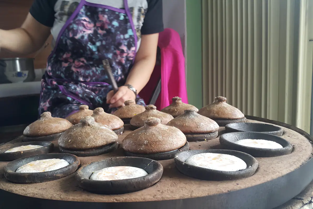 Người bán đổ bánh căn trên bếp khuôn đất nung tròn, mỗi khuôn nhỏ có nắp đất đậy, ở trung tâm Đà Lạt