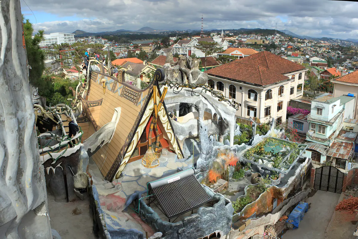 Winding rooftop walkways of the Crazy House in Da Lat, looking over its buildings and the city toward distant hills