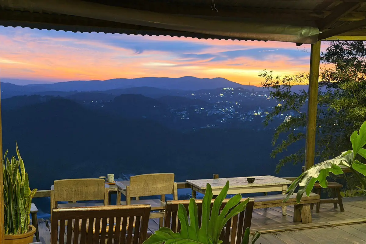 The wooden deck at Cheo Veooo at dusk, wooden tables facing the valley as Da Lat’s lights come on under a pink and orange sky