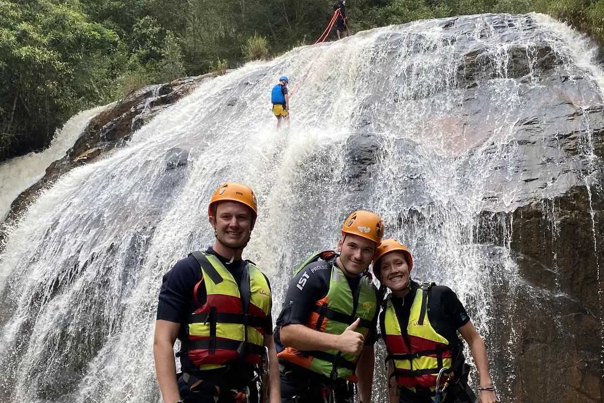 Người tham gia canyoning đội mũ, mặc áo phao và đeo đai cạnh thác nước