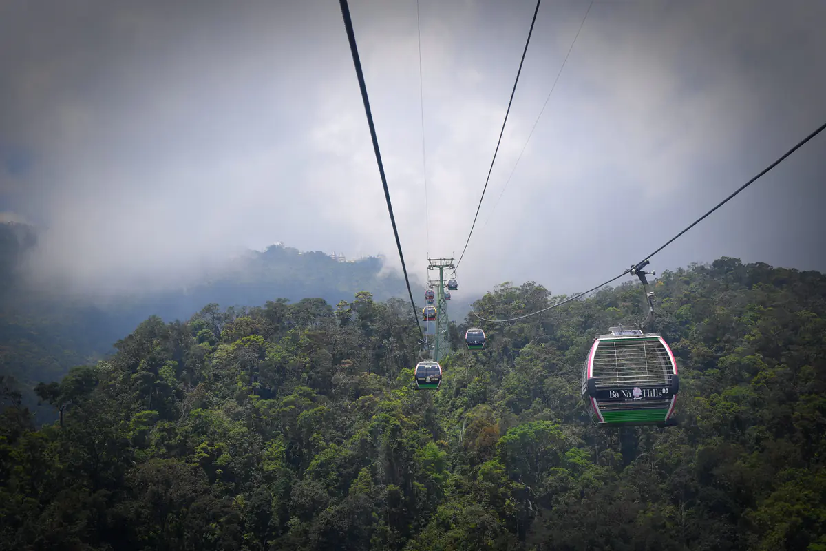 Cabin cáp treo Bà Nà Hills treo trên dây cáp băng qua rừng rậm, phía trước là trụ cáp và đỉnh núi chìm trong mây xám, khoảng 10 giờ sáng tháng 5/2017