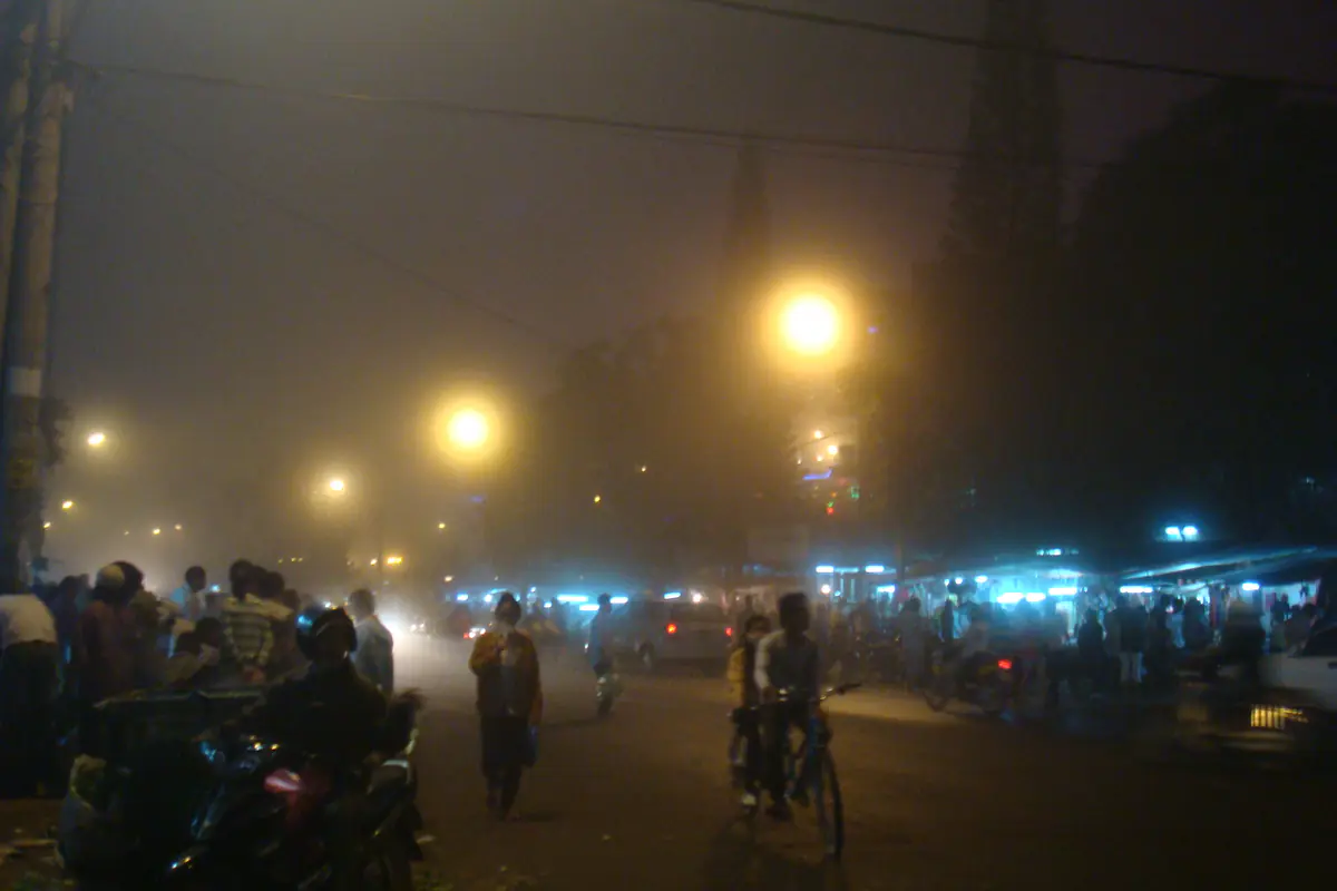 Sương mù phủ con đường dẫn vào chợ đêm Đà Lạt, đèn đường vàng và dãy sạp sáng đèn phía xa