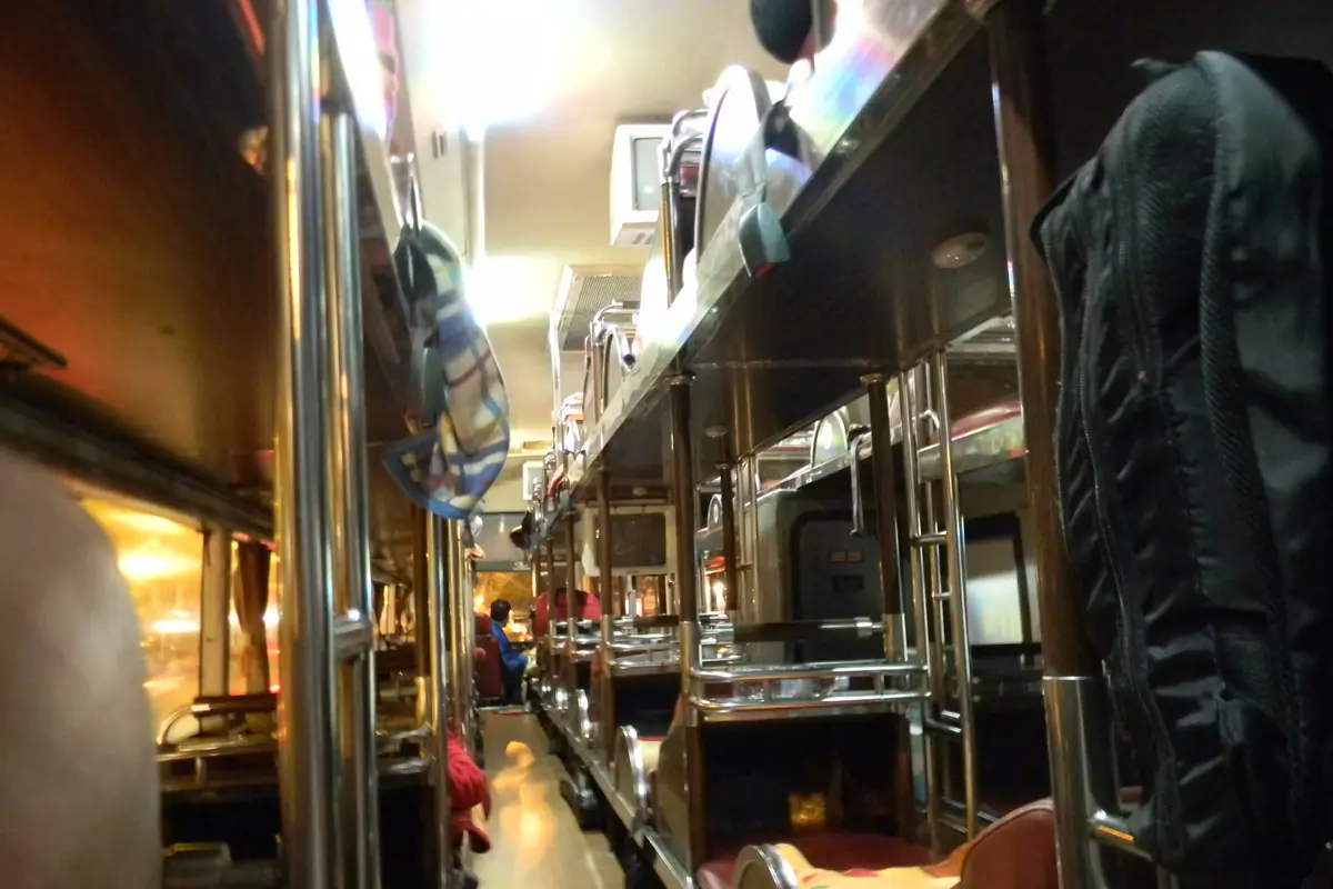The aisle between two rows of bunk berths on an overnight sleeper bus in Vietnam, with the ceiling lights on