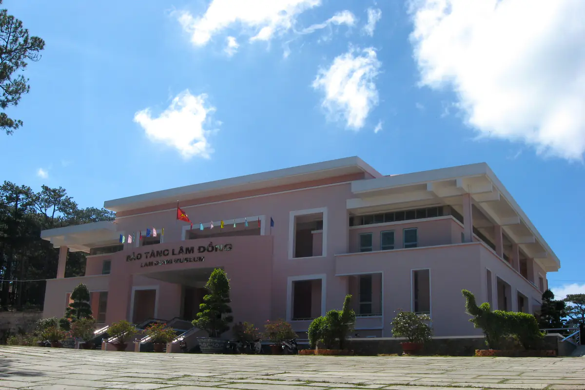 Tòa nhà chính Bảo tàng Lâm Đồng sơn màu hồng nhạt với sân lát đá và cây cảnh phía trước