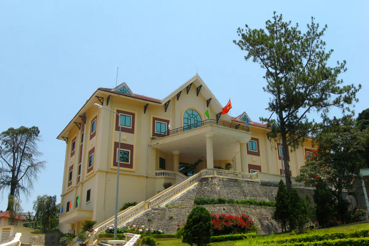 Tòa nhà chính của Biệt điện Trần Lệ Xuân sơn vàng kem, có cầu thang đá dẫn lên và rặng thông bên cạnh