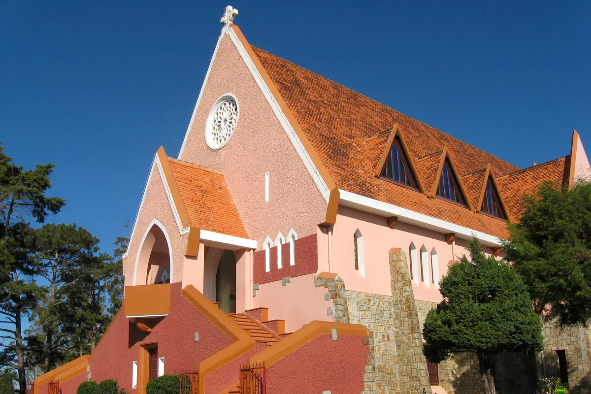 Nhà thờ Domaine de Marie ở Đà Lạt với tường hồng, mái ngói đỏ cam dốc đứng và cầu thang hai bên dưới trời xanh