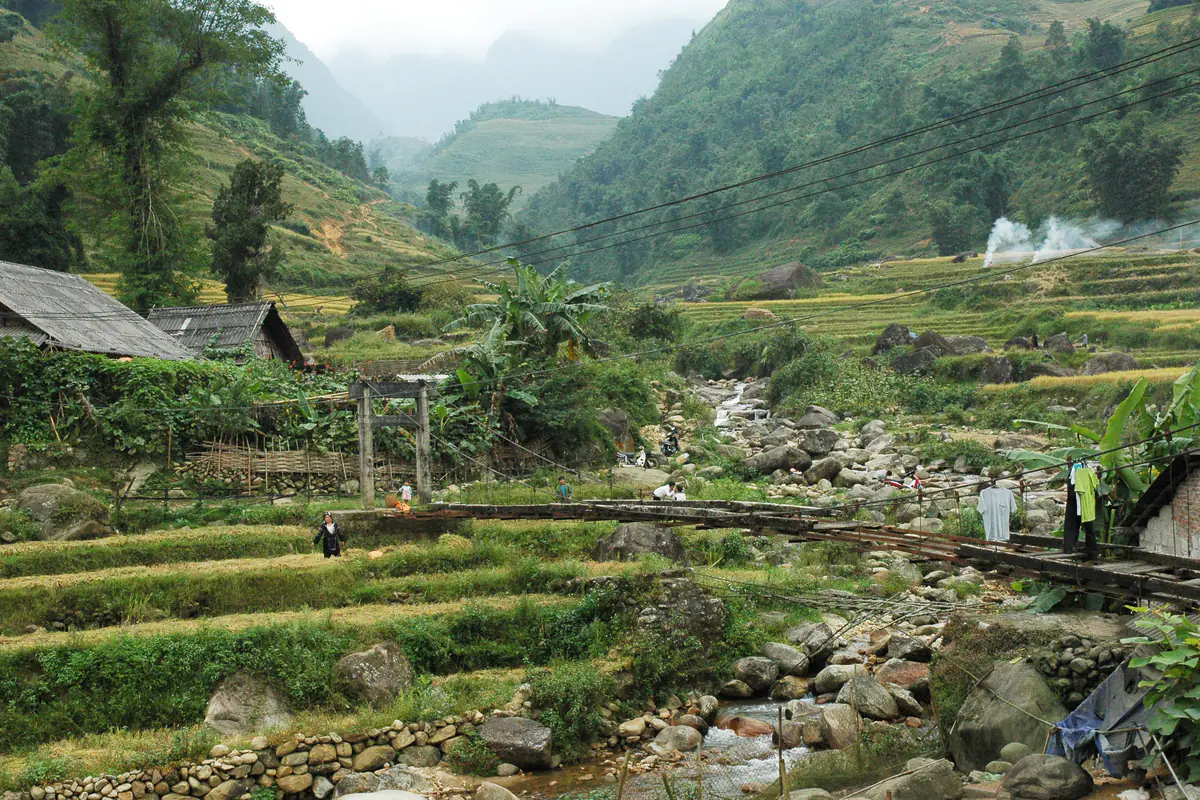 Cầu treo bằng gỗ bắc qua dòng suối đá trong một bản ở thung lũng Mường Hoa, Sa Pa, ruộng bậc thang vàng nhạt và đồi núi mờ sương phía sau, tháng 10/2011