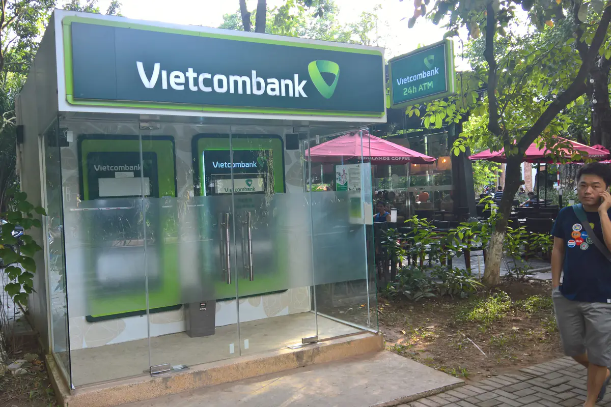 Buồng ATM kính của Vietcombank có hai máy rút tiền và biển 24h ATM, đặt dưới tán cây cạnh một quán cà phê ở khu đô thị Ecopark, gần Phố Trúc, tháng 9/2017