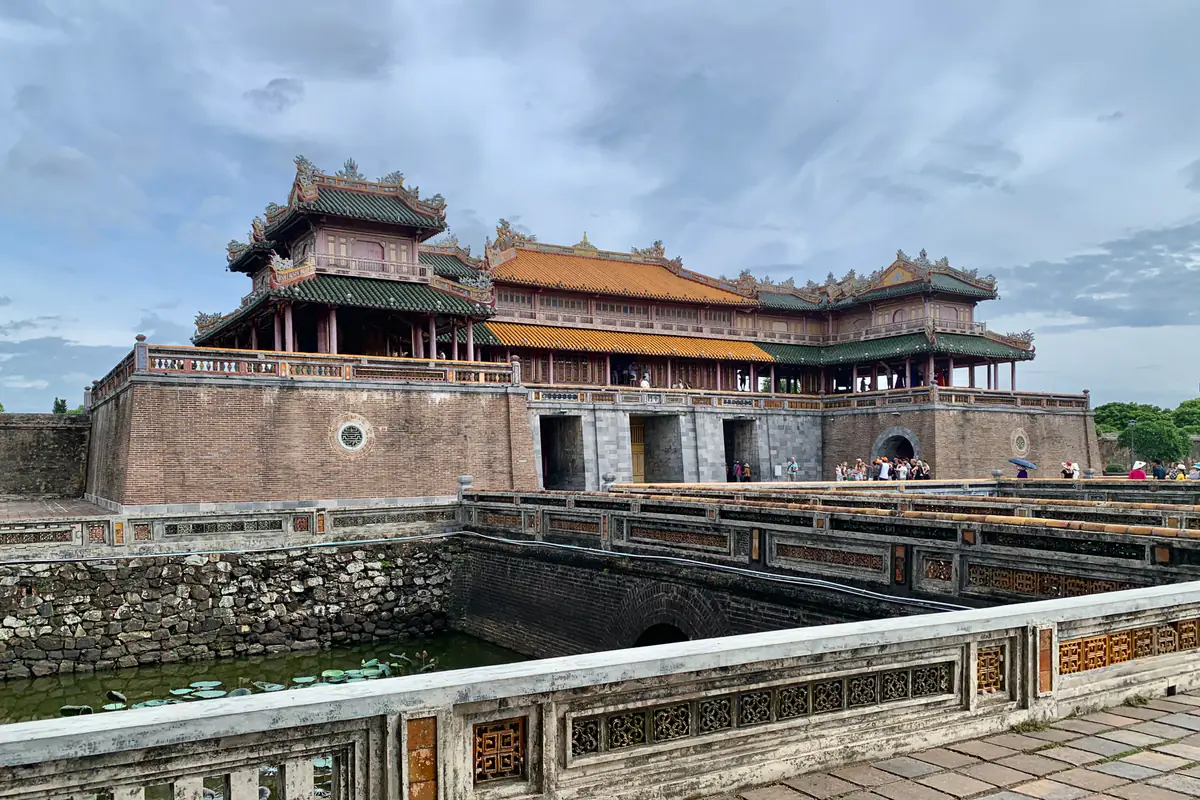 Ngọ Môn, cổng chính phía nam của Hoàng thành Huế, với lầu Ngũ Phụng mái vàng trên nền thành gạch, nhìn từ cầu đá bắc qua hồ trước cổng dưới trời nhiều mây, tháng 7/2024