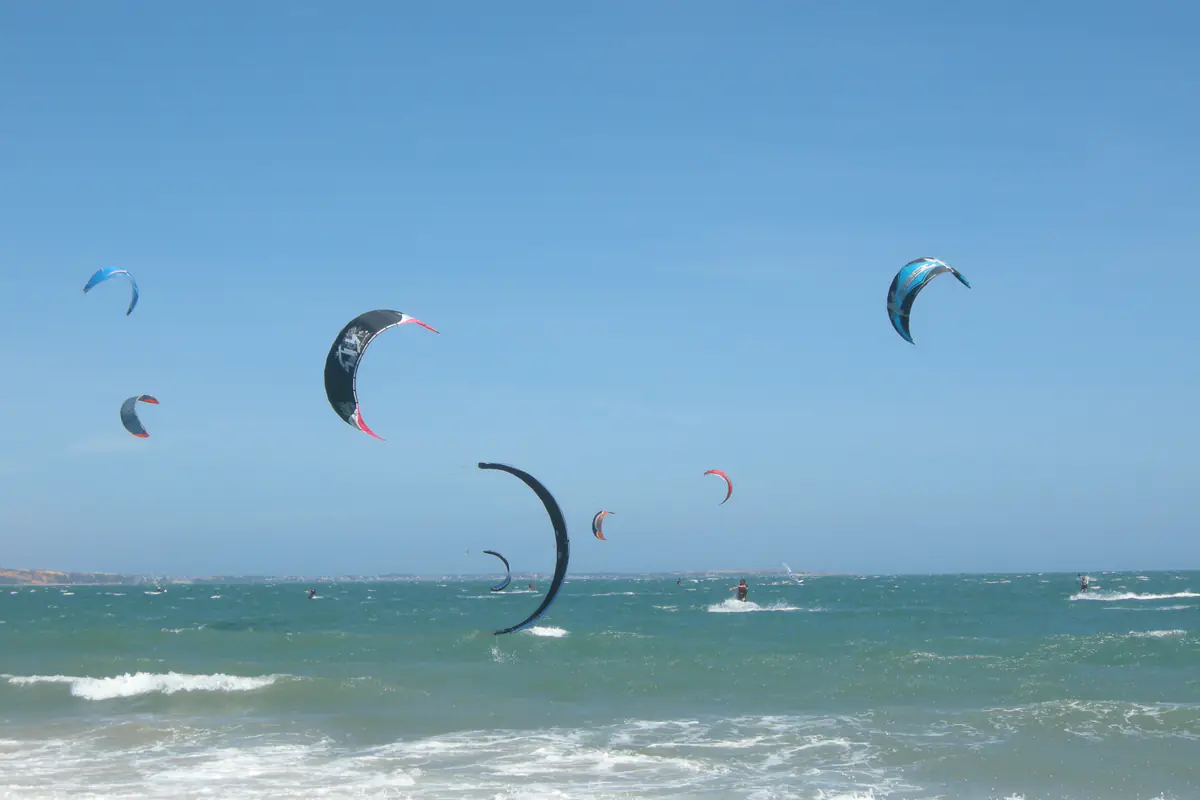 More than a dozen kitesurfing kites over Mui Ne bay on a sunny February midday in 2008, with whitecaps on a green-blue sea and a few riders near the shore