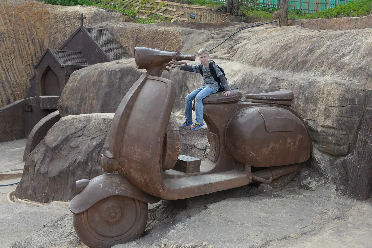 Tượng xe Vespa cổ khổng lồ bằng đất sét trong Đường hầm điêu khắc Đà Lạt, một du khách ngồi trên yên xe chụp ảnh