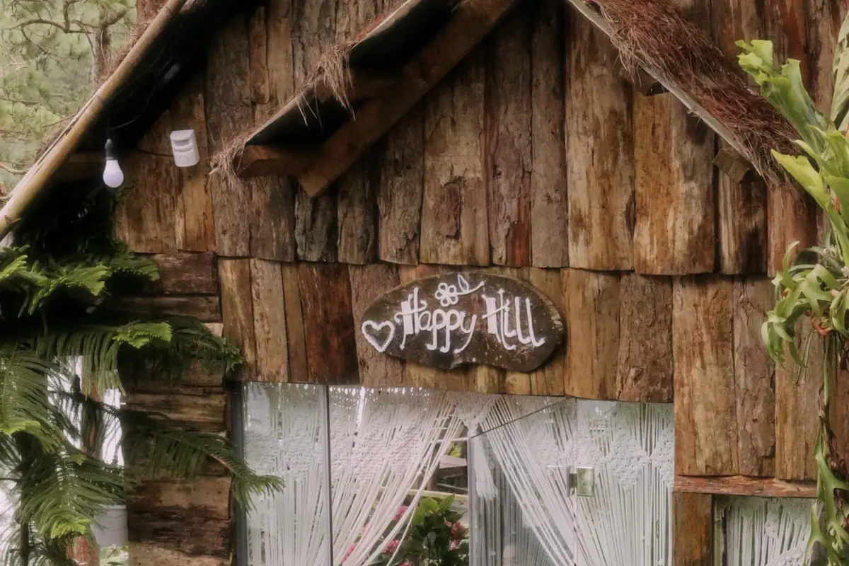 Nhà gỗ ván thô mái lá ở Happy Hill, biển “Happy Hill” treo trên cửa kính có rèm macrame trắng
