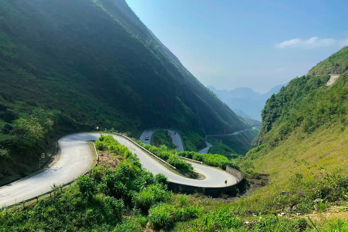 Đường nhựa uốn nhiều khúc cua tay áo giữa sườn núi phủ cỏ xanh trên dốc Thẩm Mã, quốc lộ 4C, ngày nắng mùa hè