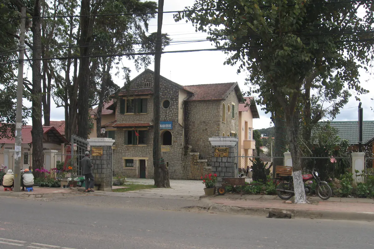 A two-story stone house with a red tile roof on a pine-lined street in the former Ward 6 of Da Lat (now Cam Ly - Da Lat Ward)