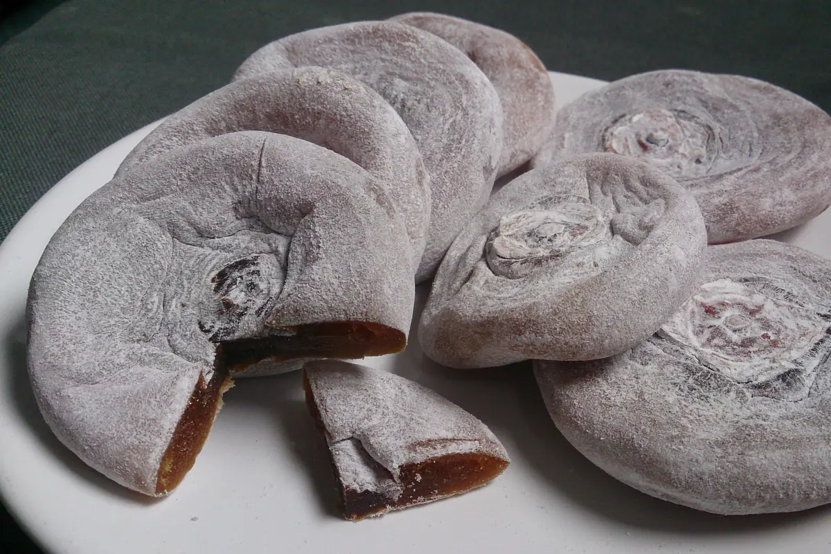 A plate of flattened dried persimmons dusted with white powder, one cut open to show the orange-brown flesh