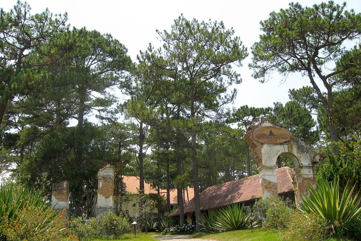 Lối đi lát đá dưới rừng thông dẫn qua cổng gạch cũ có biển Ana Mandara Villas Dalat, mái ngói nâu phía sau, năm 2011