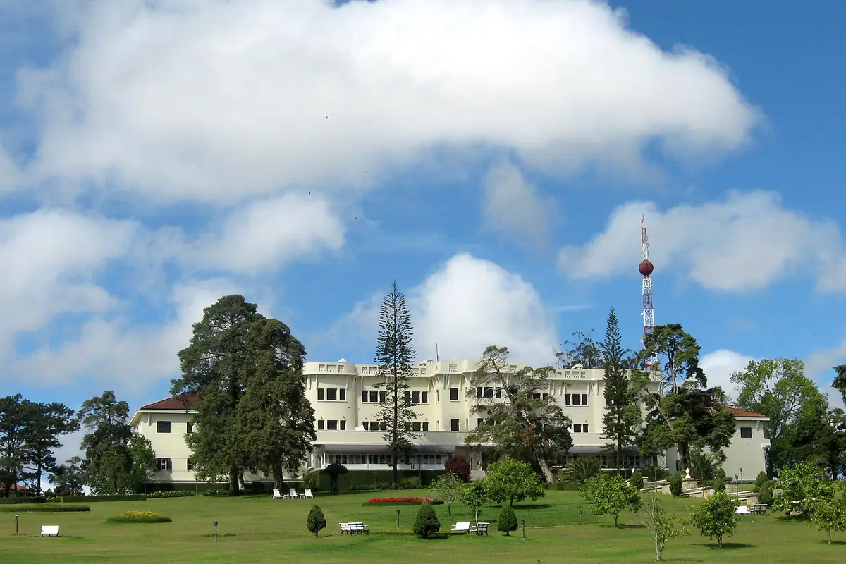 Khách sạn Dalat Palace nhìn từ bãi cỏ phía dưới, ghế trắng rải trên cỏ, hàng thông và cột ăng ten phía sau, năm 2011