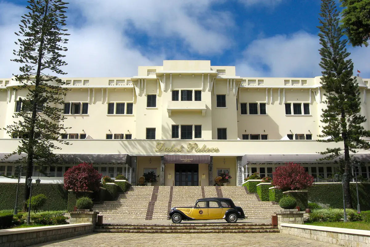 Mặt tiền khách sạn Dalat Palace màu kem với bậc thềm rộng, hai cây thông và chiếc xe cổ đỗ trước sảnh, năm 2011