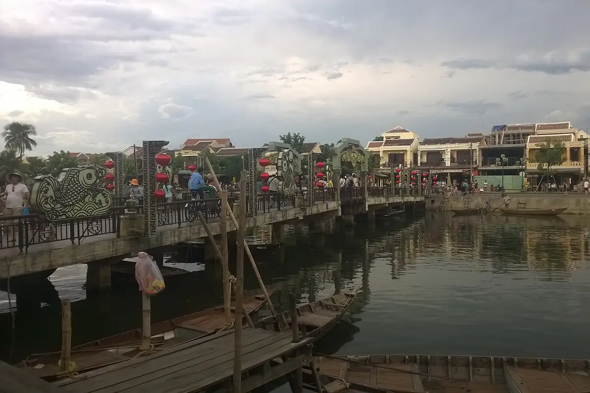 Sông Hoài lúc mực nước bình thường nhìn từ đường Bạch Đằng, cây cầu đi bộ treo đèn lồng đỏ bắc qua sông, ghe gỗ neo dưới bến và dãy nhà vàng bên kia sông, chiều nhiều mây tháng 8/2015