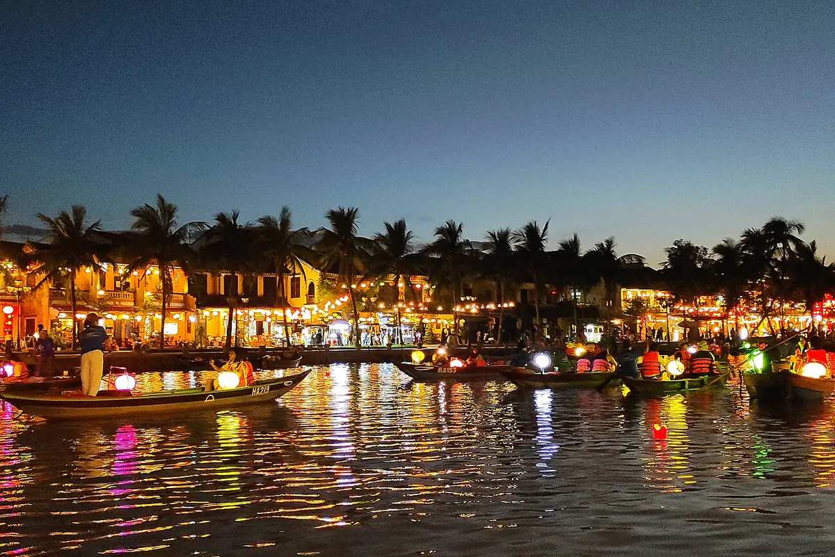 Sông Hoài lúc chạng vạng đêm 14 tháng 10 âm lịch, những chiếc ghe gỗ treo đèn lồng chở khách mặc áo phao, hoa đăng trôi trên mặt nước phản chiếu ánh đèn từ dãy nhà và hàng dừa bên bờ phố cổ Hội An, tháng 11/2022