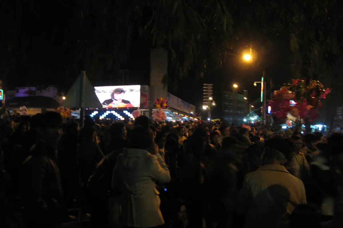 A crowd in warm jackets watching a large outdoor screen in the Hoa Binh area of central Da Lat on the evening of December 31, 2011