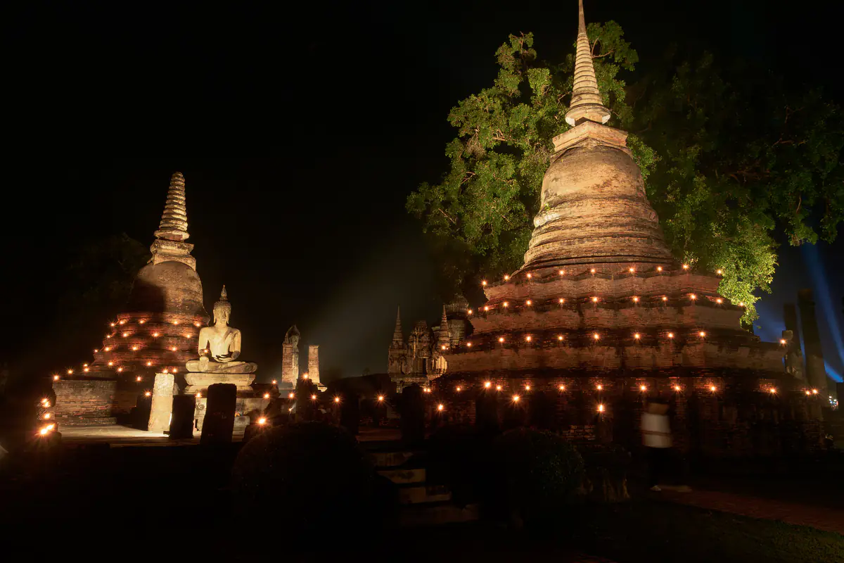 Tháp cổ và tượng Phật ngồi ở chùa Mahathat, công viên lịch sử Sukhothai, viền nến quanh các tầng tháp trong đêm lễ Loy Krathong, tháng 11/2024