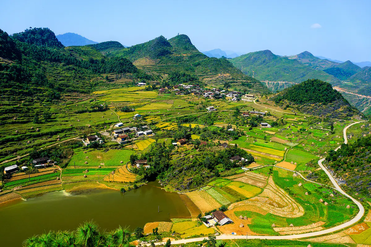 Ruộng bậc thang lúa đang chín vàng xen những thửa còn xanh quanh một hồ nước nhỏ ở Hà Giang, phía sau là dãy núi đá dưới bầu trời xanh trong, cuối tháng 9/2012