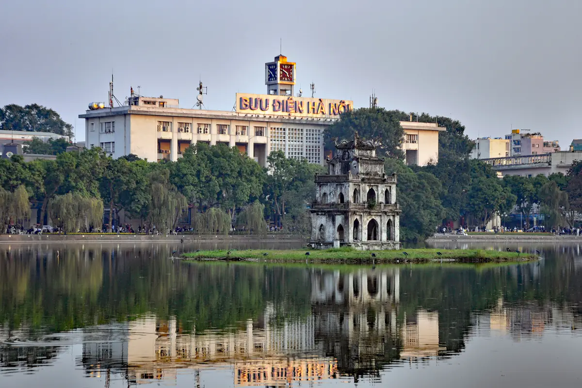 Tháp Rùa giữa hồ Hoàn Kiếm, phía sau là tòa nhà Bưu điện Hà Nội, mặt hồ phẳng in bóng, năm 2014