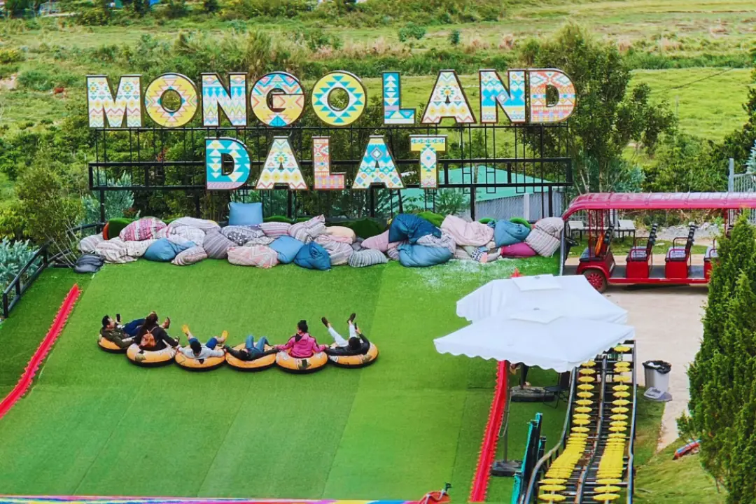 Visitors on tubes lined up on the artificial-grass slide, with the Mongo Land Dalat letters and bean-bag seating behind