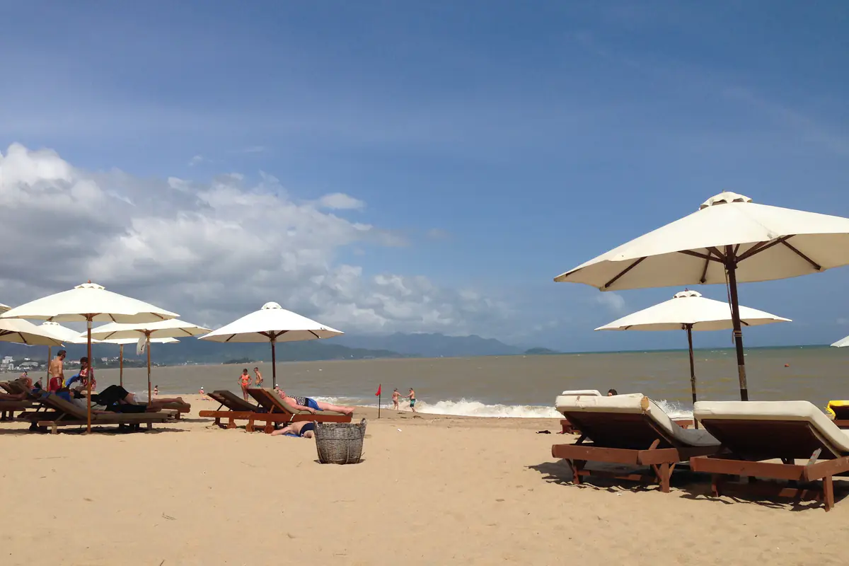Bãi tắm ở trung tâm Nha Trang với dù trắng và ghế tắm nắng, một lá cờ đỏ cắm sát mép sóng, nước biển màu nâu đục, trưa tháng 11/2013