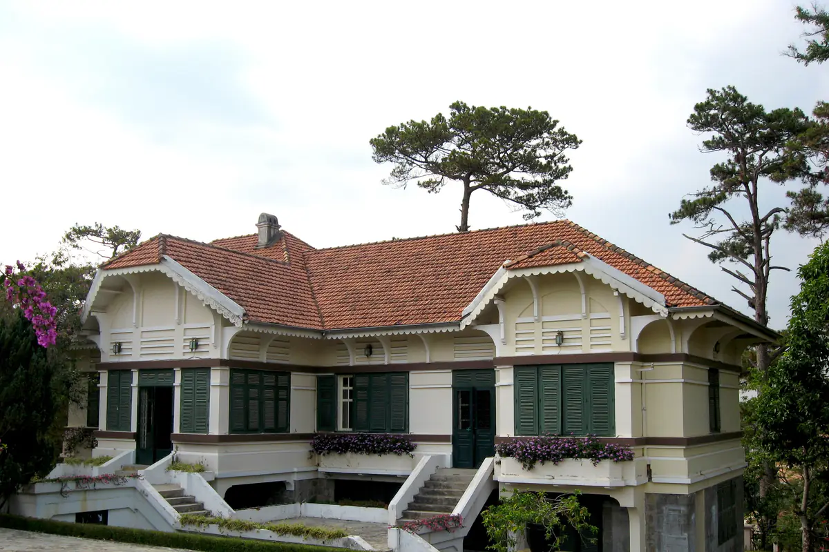 Biệt thự kiểu Pháp trên đường Trần Hưng Đạo, Đà Lạt với tường kem, cửa chớp xanh rêu, mái ngói đỏ và hàng thông phía sau