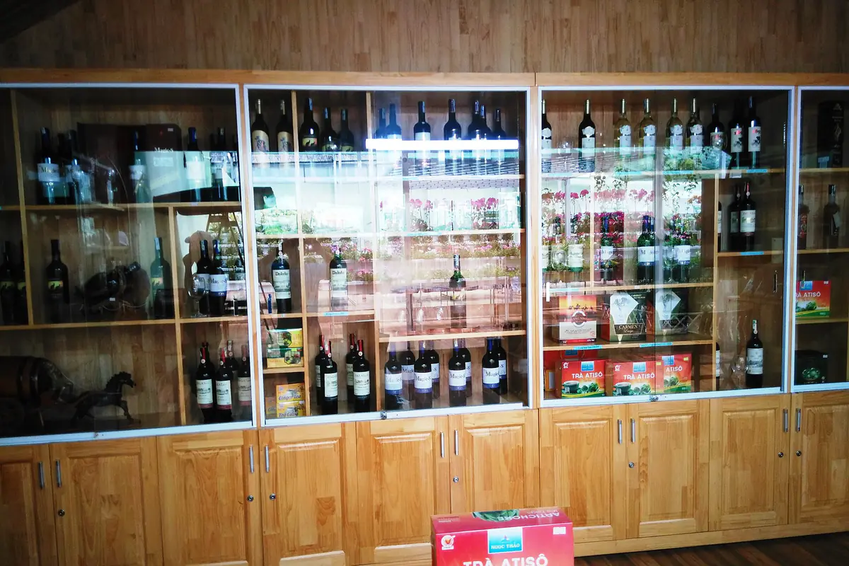 Tủ kính gỗ bày nhiều chai rượu vang cạnh hộp trà atisô ở một cửa hàng đặc sản tại Đà Lạt