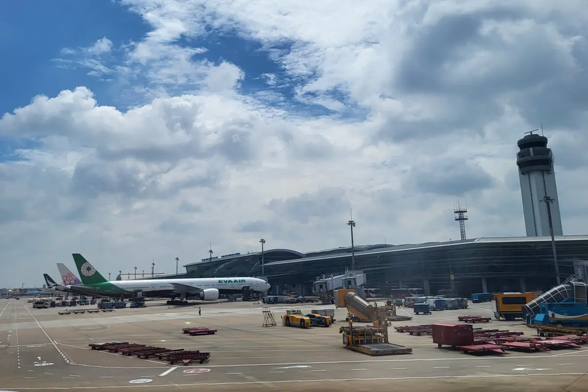 Nhà ga quốc tế T2 sân bay Tân Sơn Nhất nhìn từ sân đỗ, máy bay EVA Air đậu cạnh ống lồng, tháp kiểm soát không lưu bên phải và trời nhiều mây, tháng 8/2026