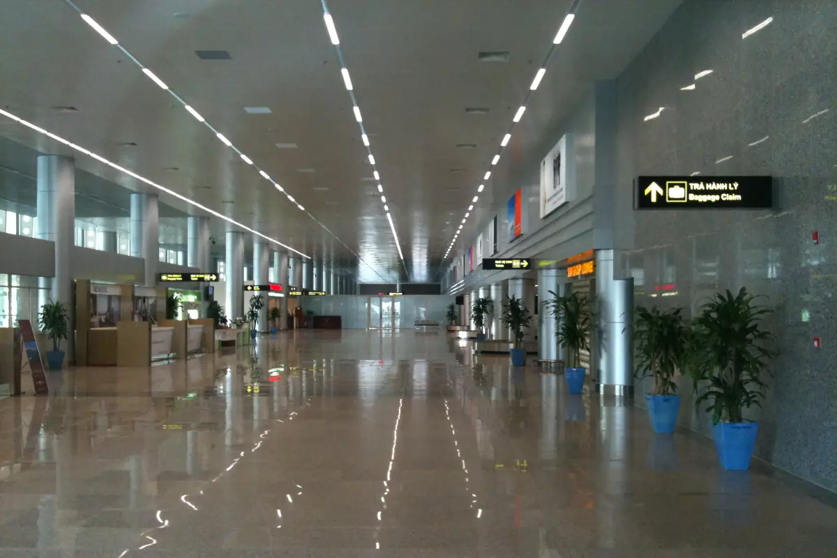 Sảnh đến nhà ga sân bay Đà Nẵng với dãy quầy dịch vụ bên trái, biển chỉ dẫn Trả hành lý - Baggage Claim bên phải và chậu cây dọc lối đi, tháng 3/2012