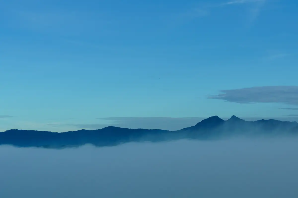 A thick white sea of fog filling the valley below a dark blue mountain ridge and a clear sky, seen from the Trai Mat area of Da Lat