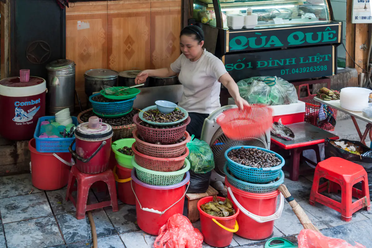 Người bán hàng ốc trên phố Đinh Liệt, Hà Nội, bên những chồng rổ nhựa đựng ốc, xô nhựa đỏ và ghế nhựa thấp trên vỉa hè, tháng 5/2011