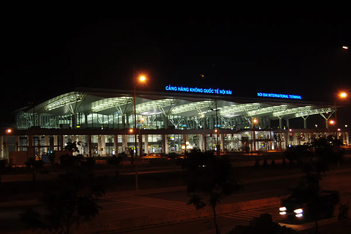 Nội Bài Airport's Terminal 2 international terminal at night, its lit steel canopy bearing the signs Cảng hàng không quốc tế Nội Bài and Noi Bai International Terminal, with the access road in front, late December 2014