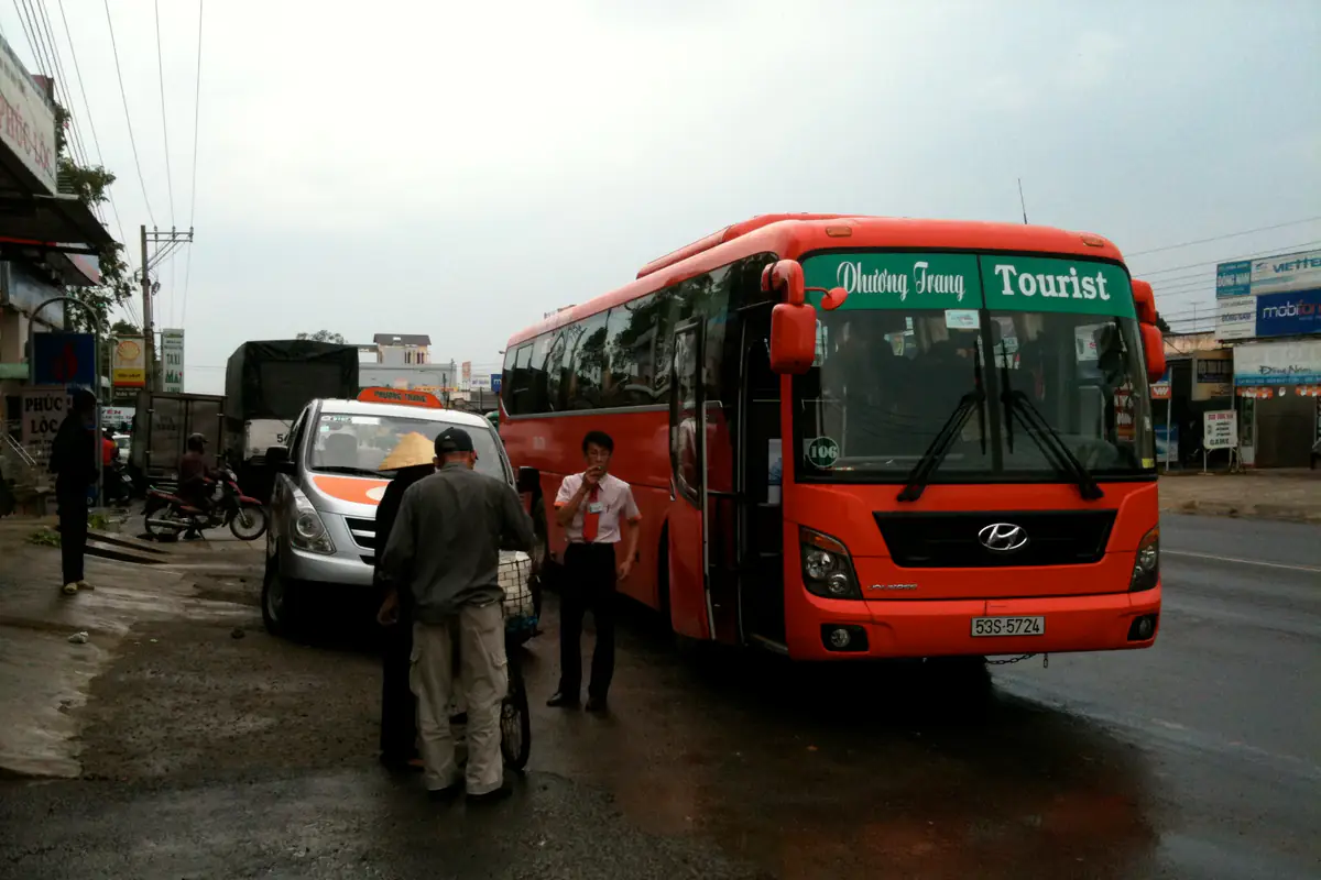 Xe khách Phương Trang màu đỏ cam dừng đón khách bên quốc lộ ở Lâm Đồng trong một ngày mưa