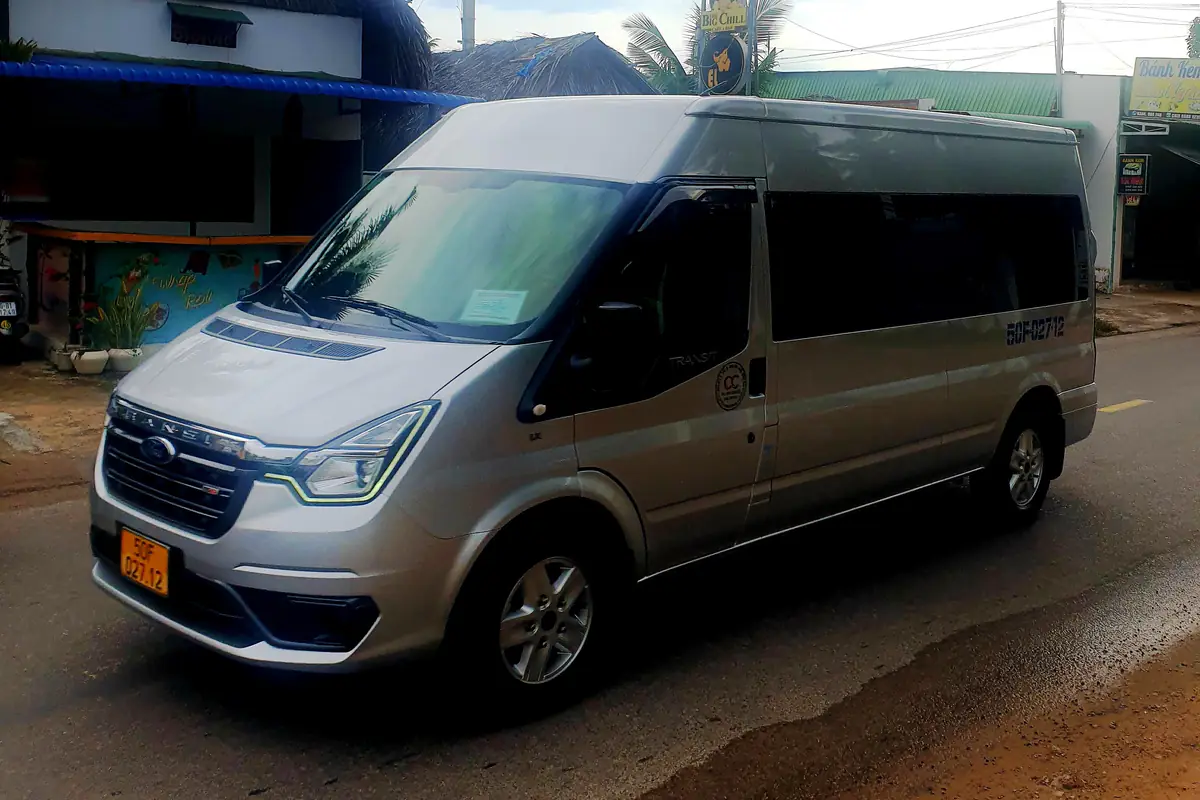 Xe khách Ford Transit màu bạc, biển số nền vàng, kính hông tối màu, đỗ bên đường ở Phan Thiết